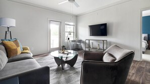 A modern living room with a sofa, armchair, glass coffee table, and a flat-screen TV mounted on the wall. - Landing | Stylish 2BD, Gym, Tennis Court (Stockbridge)
