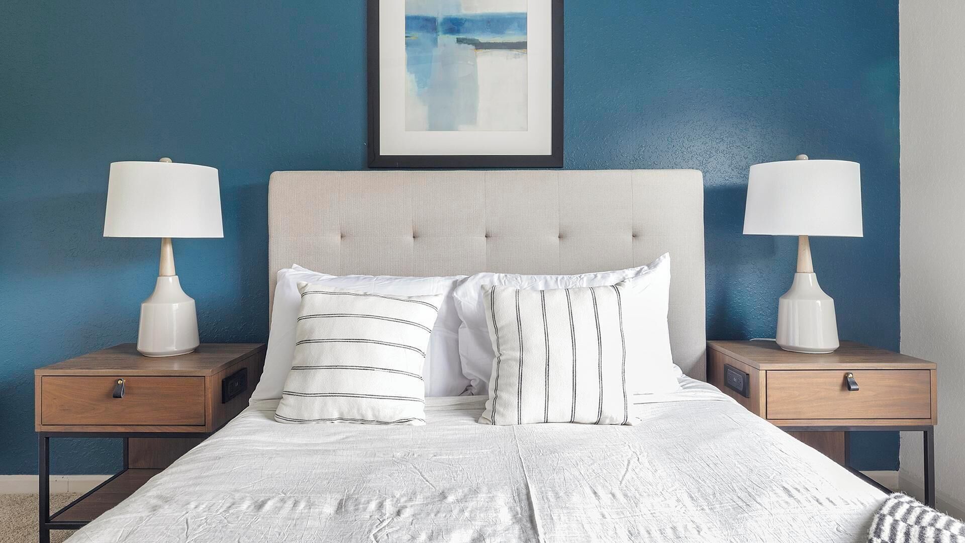 A bedroom with a tufted headboard, two bedside tables with lamps, and a bed with white bedding.