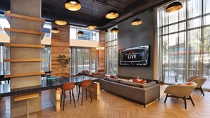 Et moderne loungeområde med bar, siddepladser og et fjernsyn, der viser en live-begivenhed.