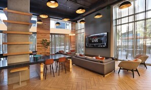 Eine moderne Lounge mit Bar, Sitzgelegenheiten und einem Fernseher, der eine Live-Übertragung zeigt.