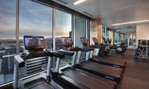 Ein modernes Fitnessstudio mit Laufbändern, Fahrrädern und Gewichten, ausgestattet mit großen Fenstern und Blick auf die Stadt.