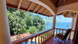 Ein Balkon mit Blick auf den Ozean, einen Pool und üppige Vegetation.