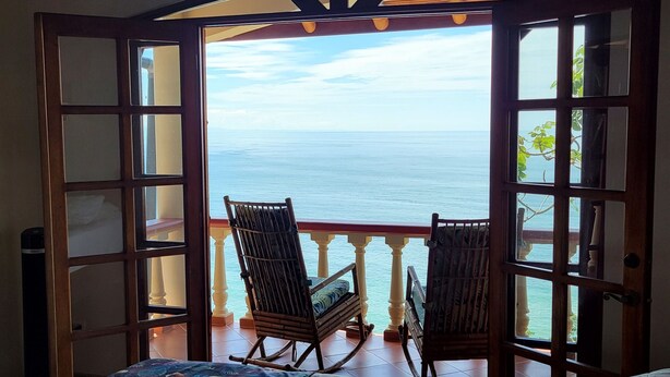 Ein Zimmer mit einem Bett, einem Schaukelstuhl und Blick auf das Meer durch eine offene Tür.