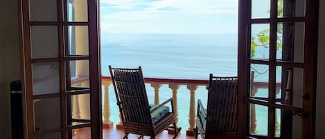 Una habitación con cama, una mecedora y vista al océano a través de una puerta abierta.