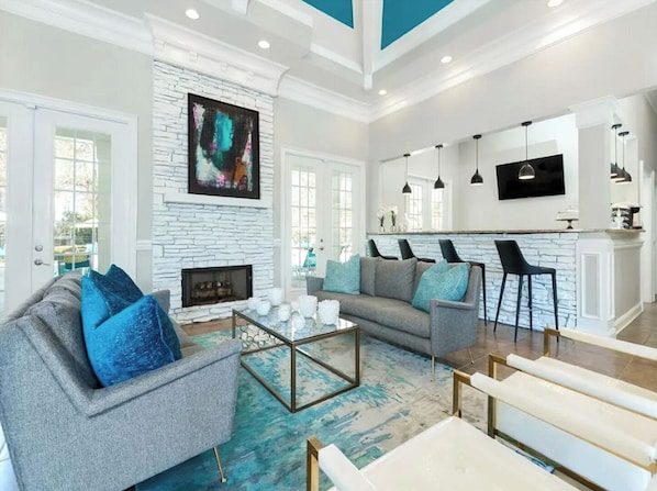 A spacious living room with a fireplace, a large abstract painting, and a kitchen area with modern appliances. - Landing | Amazing 2BD, Gym, Clubhouse (Stockbridge)