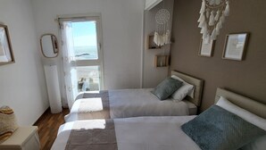 Ein Schlafzimmer mit zwei Betten, einem Fenster mit Blick, einem Traumfänger und gerahmten Bildern an der Wand.