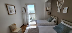 Une chambre avec deux lits, une fenêtre donnant sur un beau paysage, un attrape-rêves et des photos encadrées accrochées au mur.
