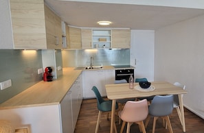 A compact kitchen with wooden cabinets, a built-in oven, and a dining area with a table and chairs. - A feast for your eyes, 3 bedroom apartment on beach, sea views from every room. (Mauguio)