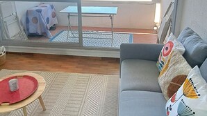 Ein Balkon mit Meerblick, eine Sitzecke mit gemusterten Kissen, ein kleiner Tisch mit einem roten Tablett und ein Teppich mit Muster.