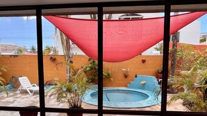 Un espace piscine agrémenté d’un auvent rouge, de plantes en pot et d’une chaise longue blanche.