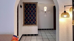 Une porte en arc surmontée d’une tapisserie à motifs, un luminaire fixé au mur et un revêtement de sol carrelé.