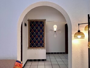 An arched doorway with a patterned tapestry, a wall-mounted light fixture, and tiled flooring. - Casa Shabat (Puerto Morelos)