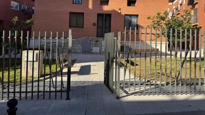A courtyard with a brick building, a metal gate, and a small tree. - Apartamentos Melisa (Madrid)