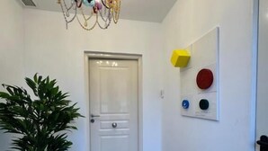 A hallway with a white door, a potted plant, a chandelier, and a wall with geometric decorations. - Apartamentos Melisa (Madrid)