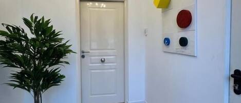 A hallway with a white door, a potted plant, a chandelier, and a wall with geometric decorations.