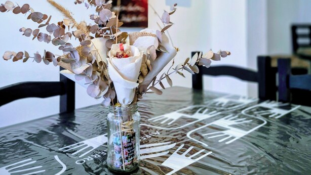A dining table with a glass vase containing dried flowers and leaves, set against a wall with two vertical banners. - Aires del Cerro House (Yerba Buena)