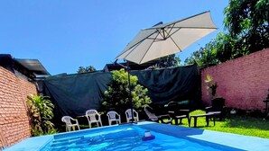 A rectangular swimming pool with clear blue water, surrounded by a brick wall, a green lawn, and outdoor furniture. - Aires del Cerro House (Yerba Buena)