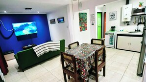 A living room with a TV, a ceiling fan, a dining table with chairs, a kitchen area with cabinets and a microwave, and a green door. - Aires del Cerro House (Yerba Buena)