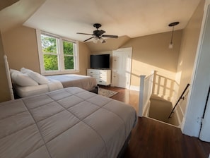 Ein Schlafzimmer mit zwei Betten, einem Deckenventilator, einem Fernseher und einer Treppe.