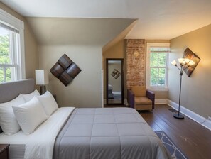 Ein Schlafzimmer mit einem Bett, einem Sessel, einer Lampe und einer Backsteinwand.