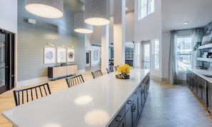 Une cuisine moderne dotée d’un grand îlot central, de luminaires suspendus et offrant une vue sur l’extérieur.