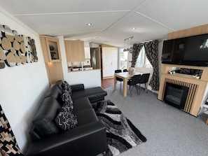 A modern living room with a black leather sofa, a dining area with a wooden table, and a TV mounted on a wooden cabinet.