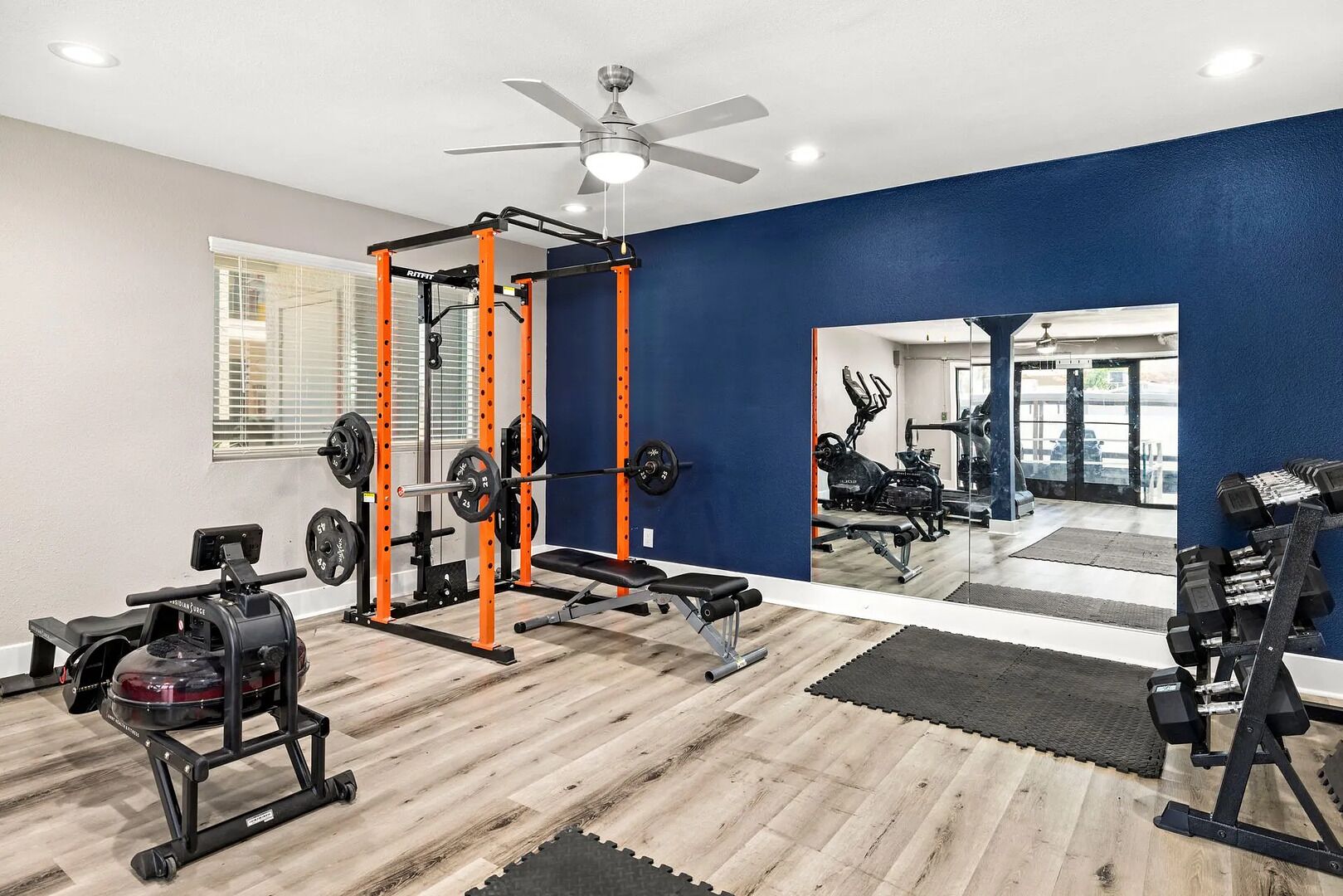 Ein Fitnessstudio mit Gewichthebereck, Trainingsgeräten und einem Spiegel, der den Raum wiederspiegelt.