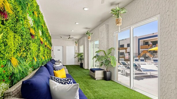Eine Hotelhalle mit grüner Wand, einem Korbssessel mit Kissen, einem Blumentopf und Blick auf den Poolbereich.