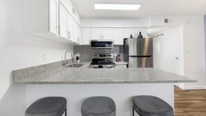 Eine moderne Küche mit weißen Schränken, einem Edelstahl-Kühlschrank, einer Mikrowelle und einer Arbeitsplatte aus Granit.
