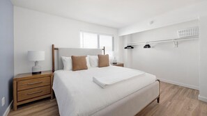 Een slaapkamer met een bed, nachtkastjes, een lamp, een raam en een wandplank.