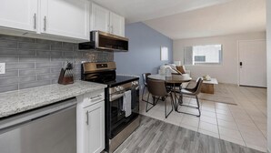 A modern kitchen with white cabinets, a stainless steel stove, and a dining area with a round table and chairs. - Landing | Incredible 2BD in Glendale (Glendale)