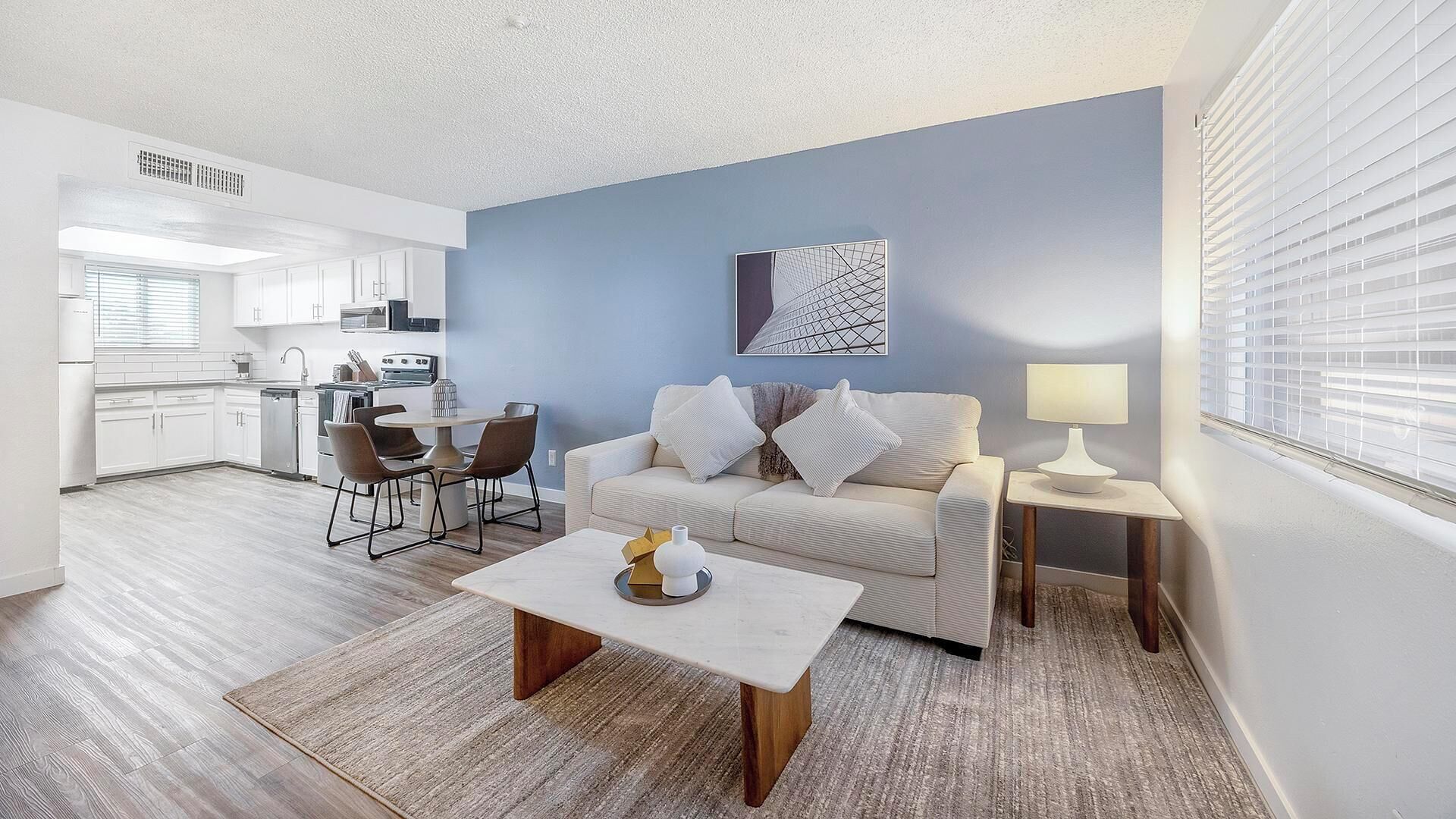 Een moderne woonkamer met een bank, salontafel en een eethoek met stoelen.
