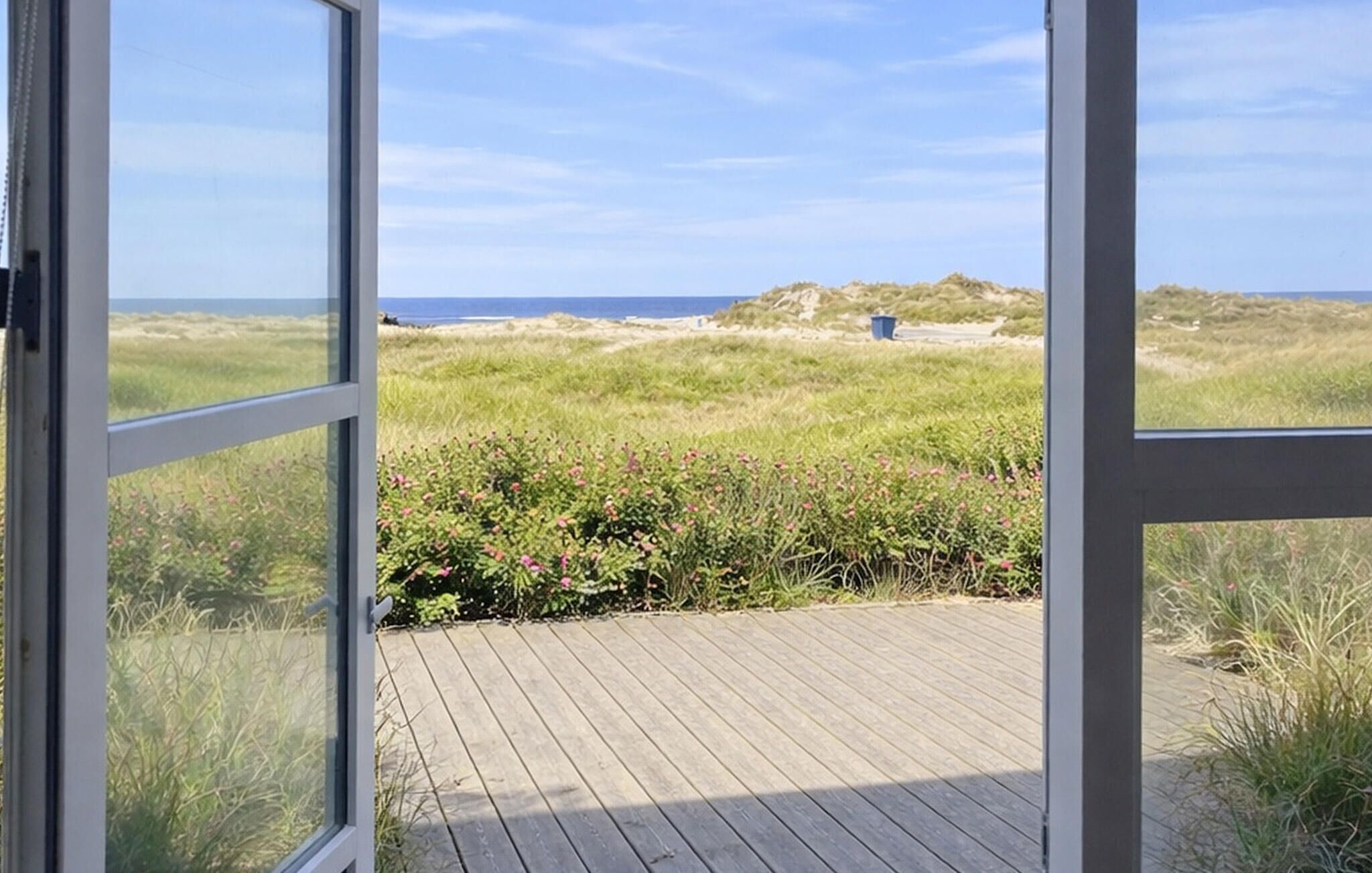 Une terrasse en bois qui mène à une plage bordée de dunes, sous un ciel dégagé.