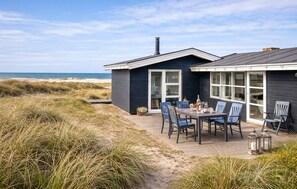 Ett hus vid kusten med en terrass, utomhusmöbler och utsikt över stranden.