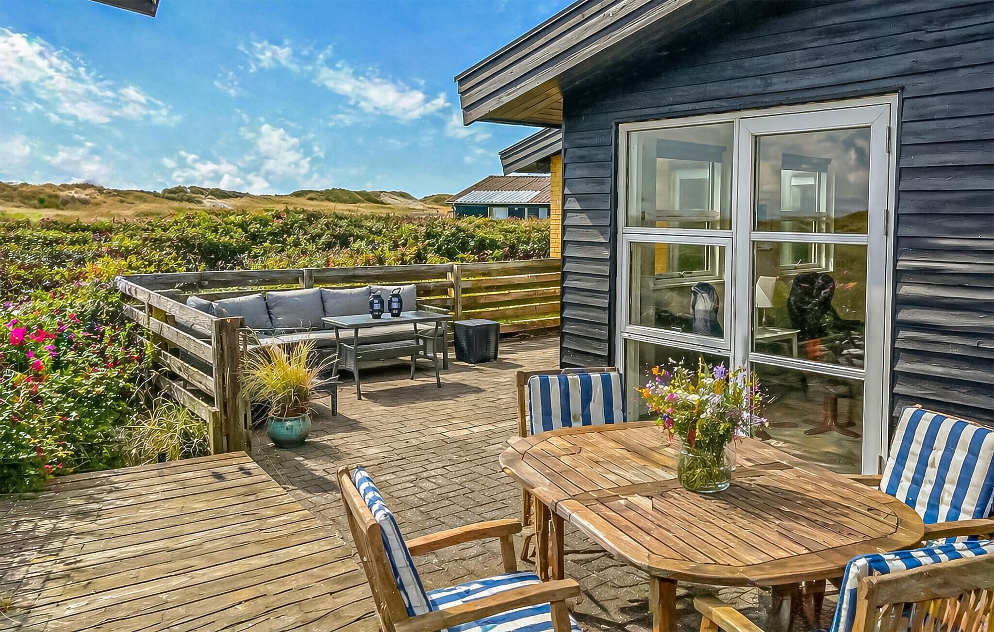 A wooden deck with outdoor furniture, a large window, and a view of the surrounding landscape.