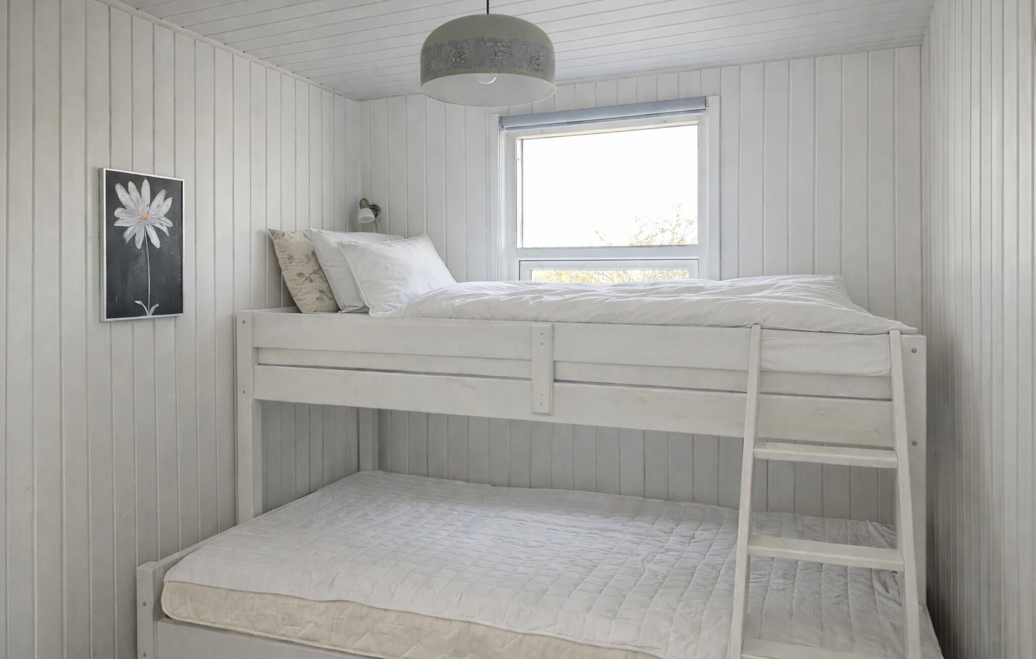 Un lit superposé avec une fenêtre au-dessus, un oreiller et un tableau accroché au mur.