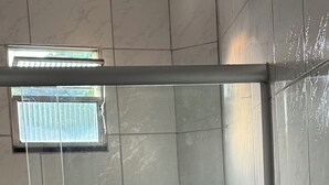 A bathroom with a glass shower enclosure, a toilet, and a shelf with toiletries. - Cozy apartment (Salvador)