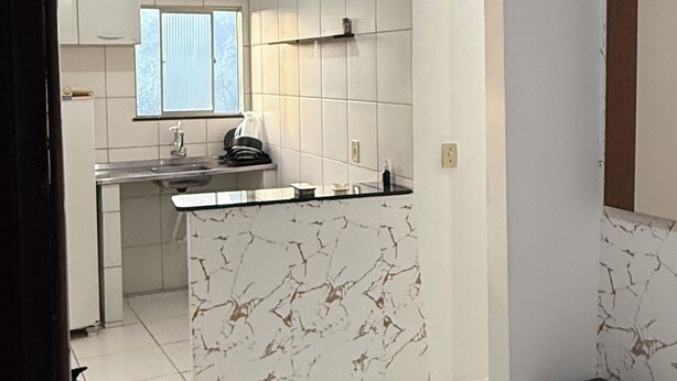 A modern kitchen with white cabinets, a marble countertop, and a black countertop. There is a window with blinds, a black countertop, and a black stool. - Cozy apartment (Salvador)