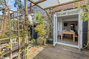 Una terraza de madera con una mesa y sillas, rodeada por un cerco de madera y plantas en macetas.