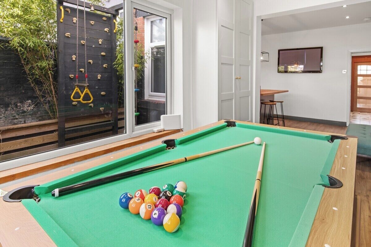A pool table with balls and a climbing wall in a room with a door and a TV.