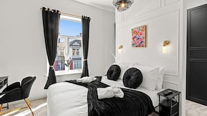 Une chambre moderne avec un lit, une literie noire et blanche, une chaise noire, une petite table de chevet et une fenêtre avec des rideaux noirs.