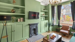 Un salon avec une cheminée, un téléviseur fixé au mur et une fenêtre avec des rideaux.