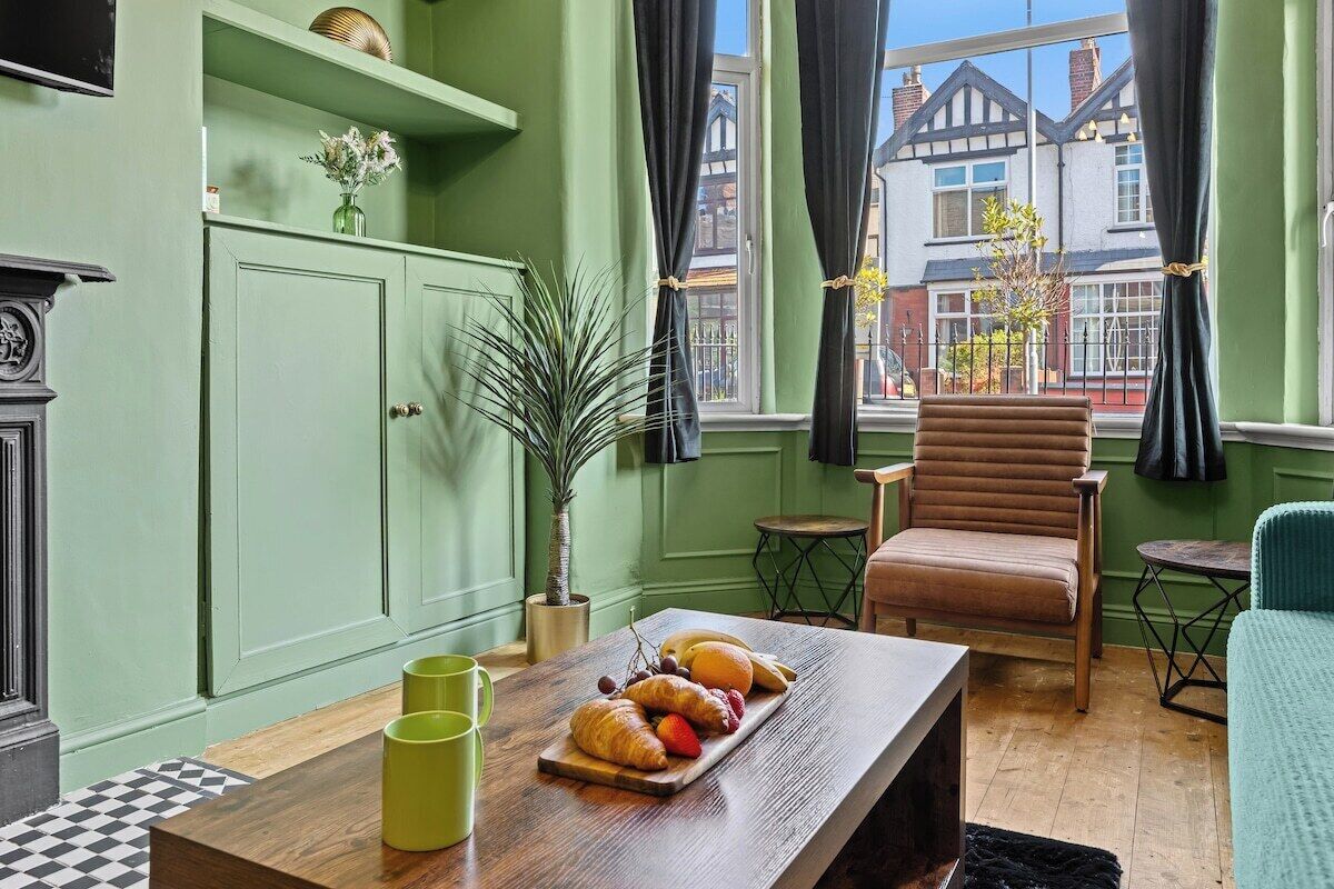 Een kamer met een groene wand, een houten tafel met eten, een stoel, een klein tafeltje en een plant.