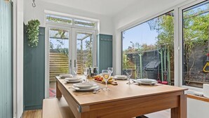 Un coin repas avec une table en bois dressée pour quatre personnes, une vue sur le jardin grâce à de grandes fenêtres et une porte donnant sur l’extérieur.