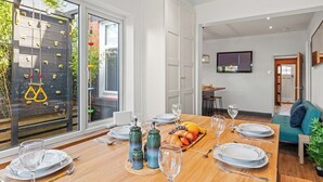 Un coin repas avec une table en bois dressée pour deux personnes, une assiette de fruits et des salières et poivrières.