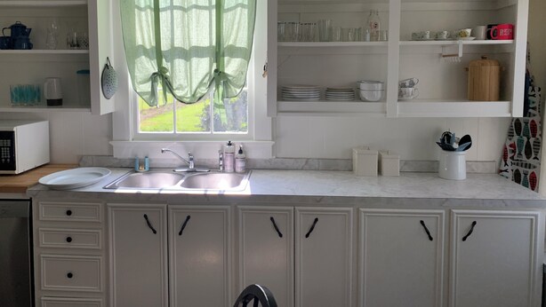 A kitchen with a window, sink, cabinets, and shelves with dishes and utensils. - The Lone Start Suite on the Mississippi River in Donaldsonville (Donaldsonville)