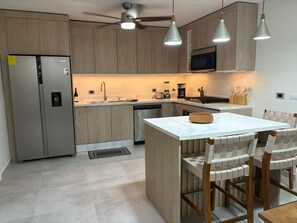 Eine moderne Küche mit Holzausstattung, Edelstahlgeräten, einer zentralen Kochinsel und Pendelleuchten.