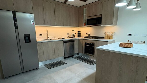 Uma cozinha moderna com ilha central, eletrodomésticos embutidos e iluminação pendente.