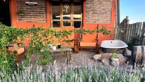A rustic building with a brick facade, a wooden door, and a window with a peace sign. There are outdoor seating arrangements and a garden with lavender. - Ranchito de Montaña a refuge designed for unique moments Casita close to everything (Lujan De Cuyo)
