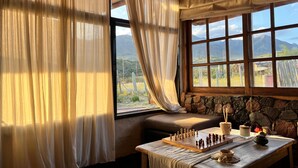 A cozy room with a stone wall, a wooden bench, a chessboard, and a view of mountains through large windows. - Ranchito de Montaña a refuge designed for unique moments Casita close to everything (Lujan De Cuyo)